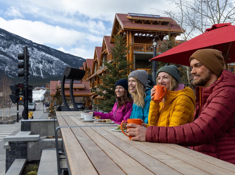 A group of friends sit on the Whitebark Cafe patio in the winter looking out at the mountains in Banff.