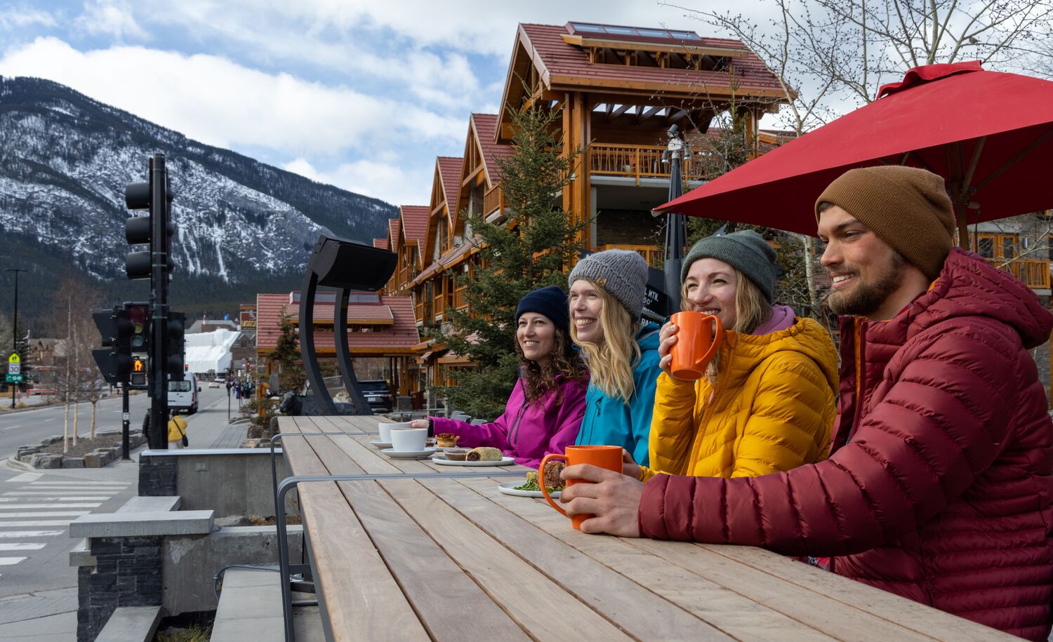 A group of friends sit on the Whitebark Cafe patio in the winter looking out at the mountains in Banff.