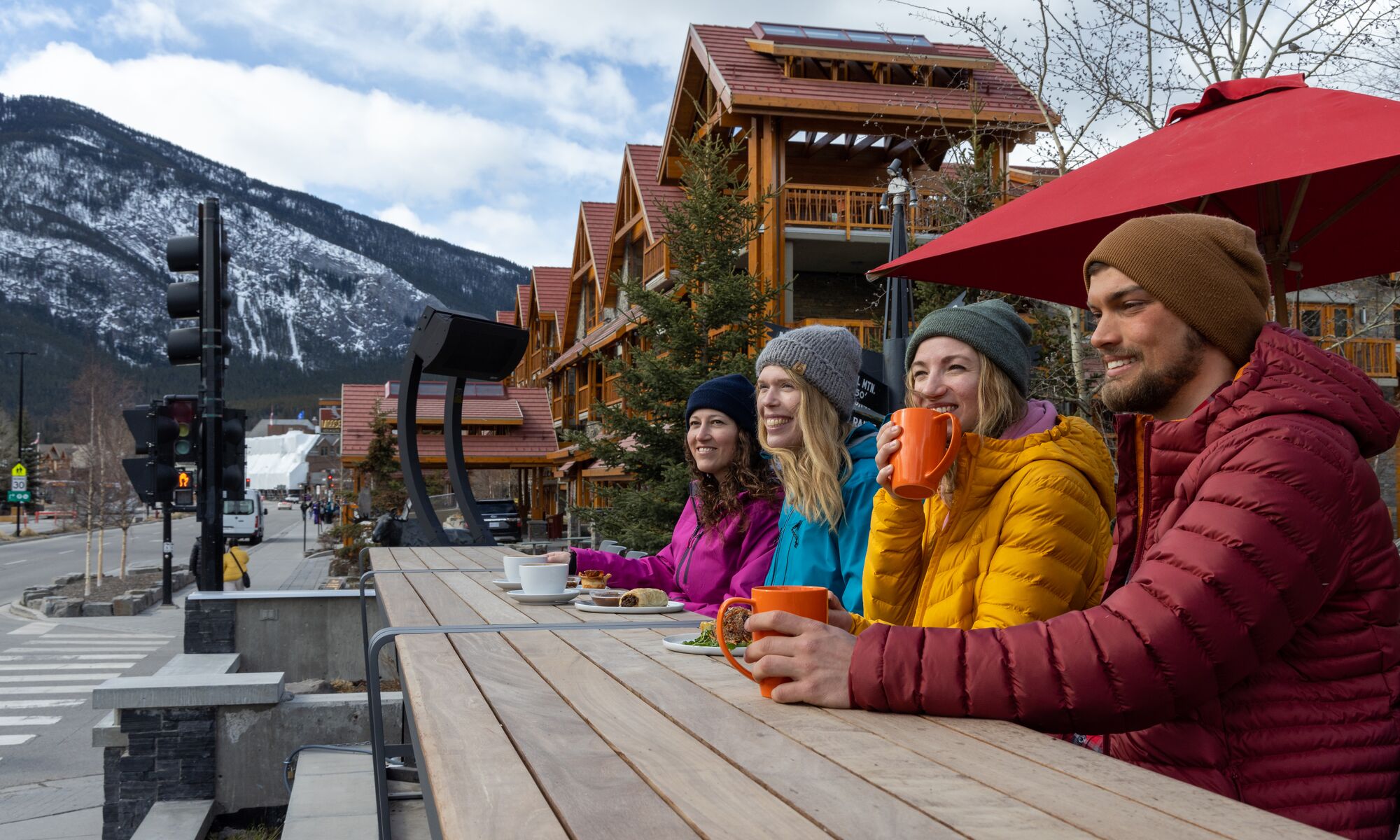 A group of friends sit on the Whitebark Cafe patio in the winter looking out at the mountains in Banff.