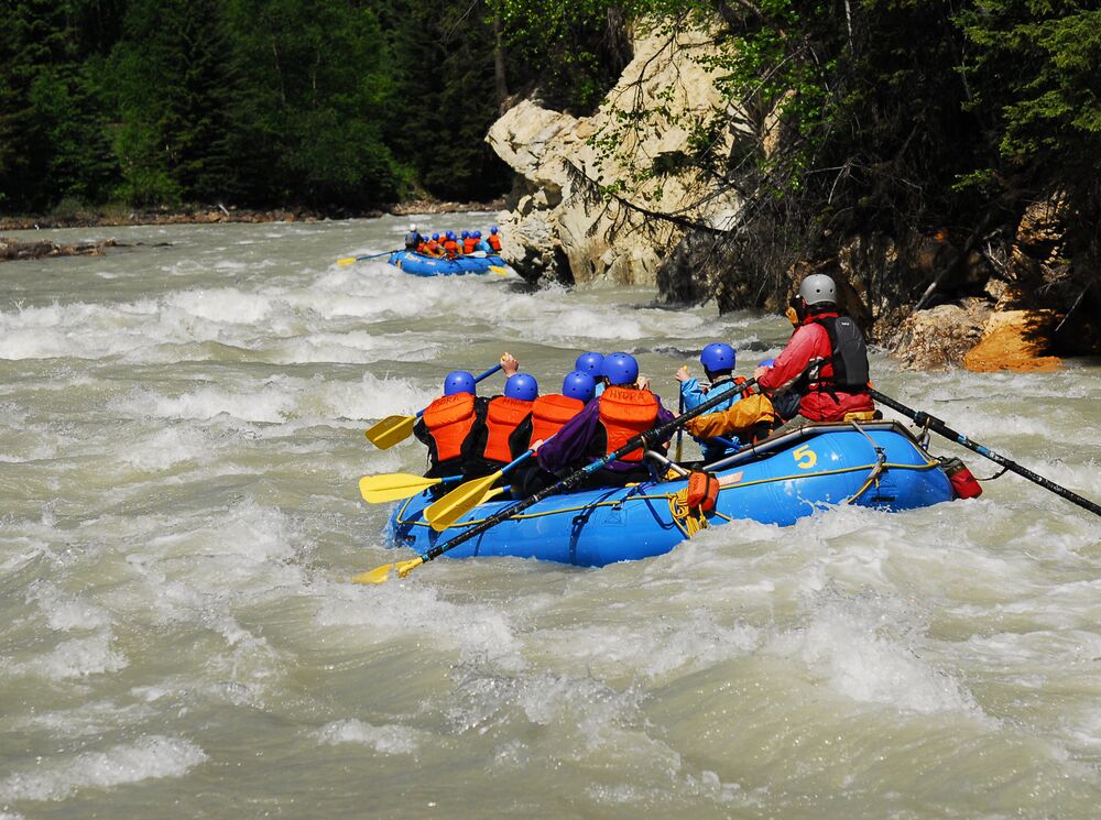 A group of people in a raft paddling through rapids on a white water rafting tour