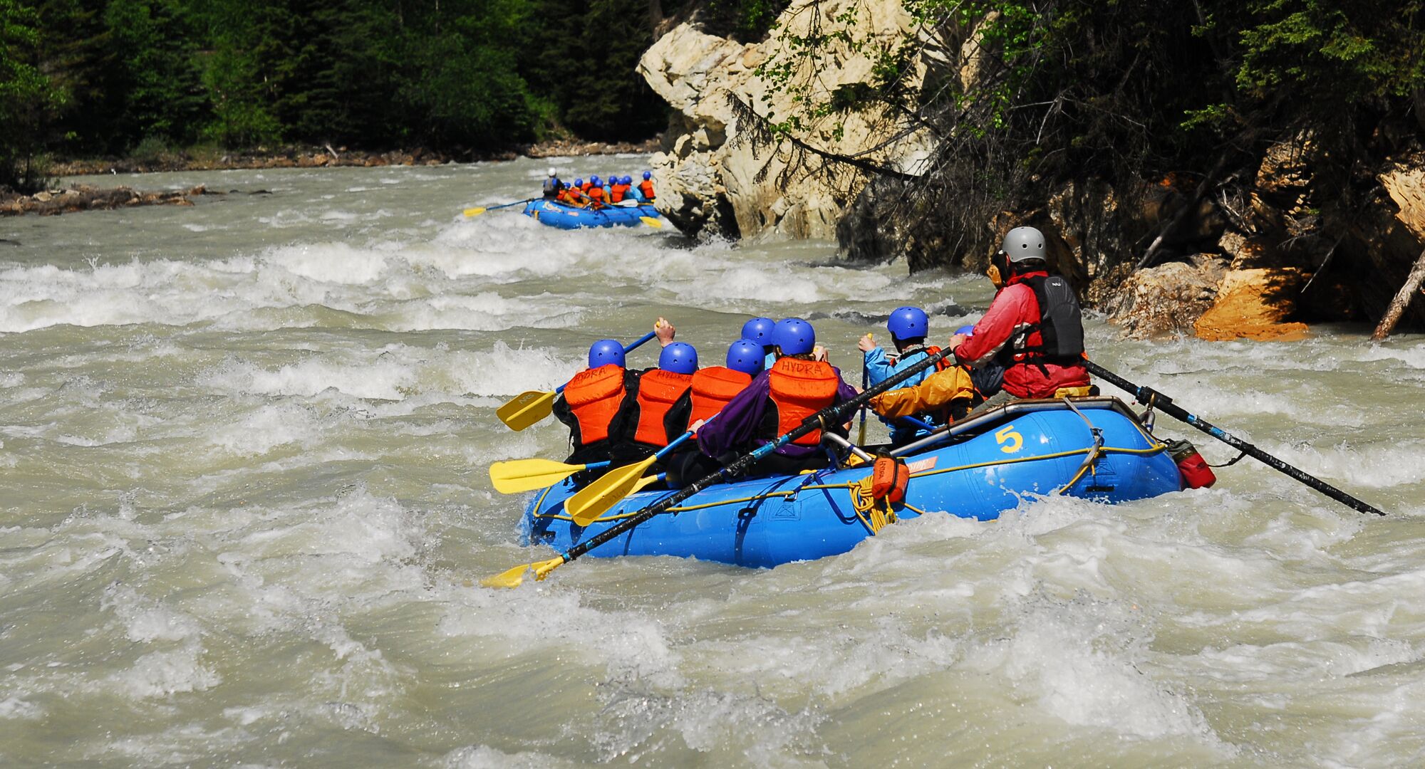 A group of people in a raft paddling through rapids on a white water rafting tour