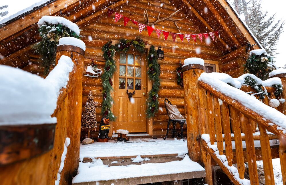 Snowy winter wood cabin with ice skates hanging outside with a welcome sign and Christmas decorations.