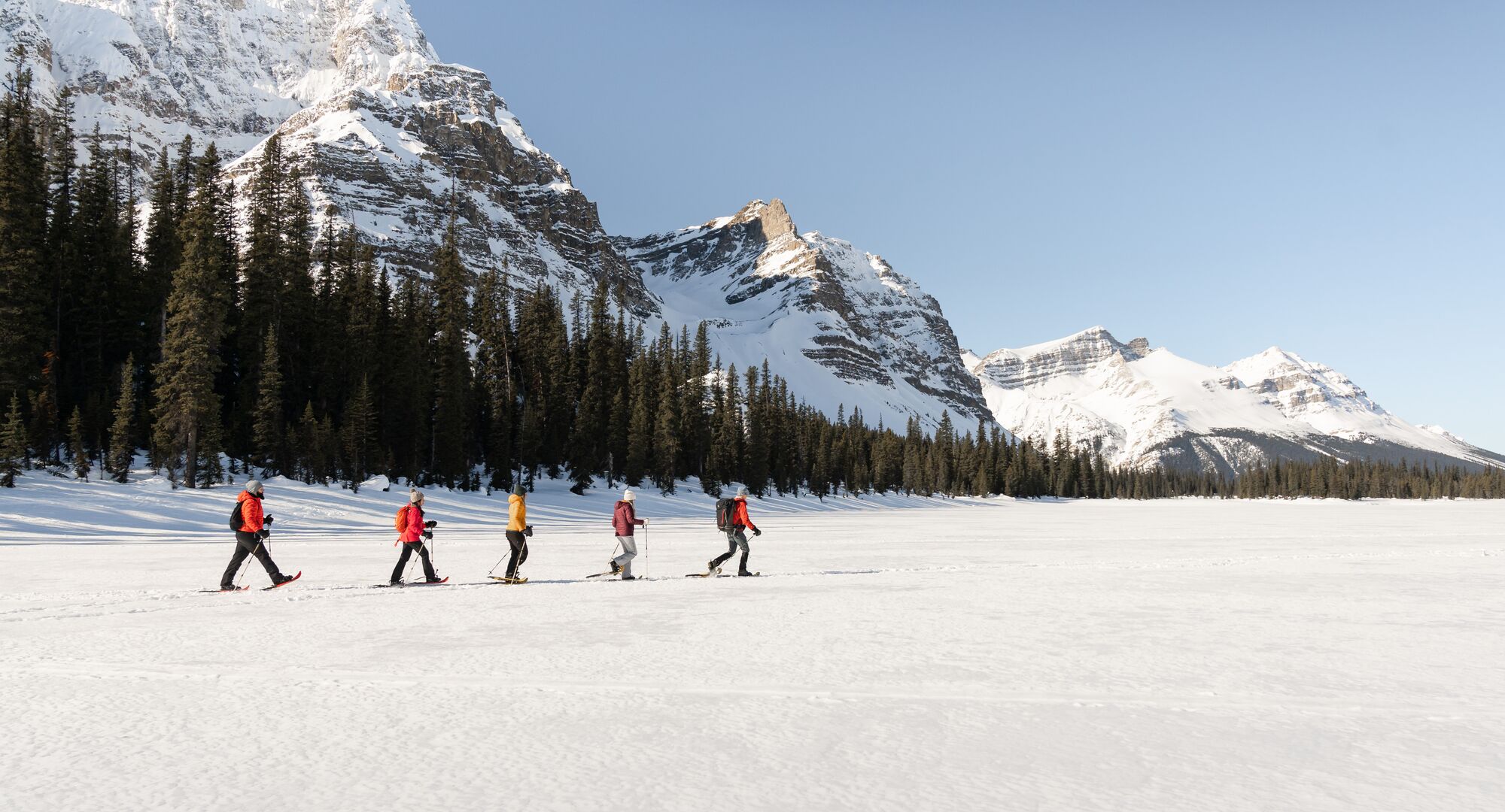 A group of people crossing a snow covered valley on snowshoes on a sunny winters day