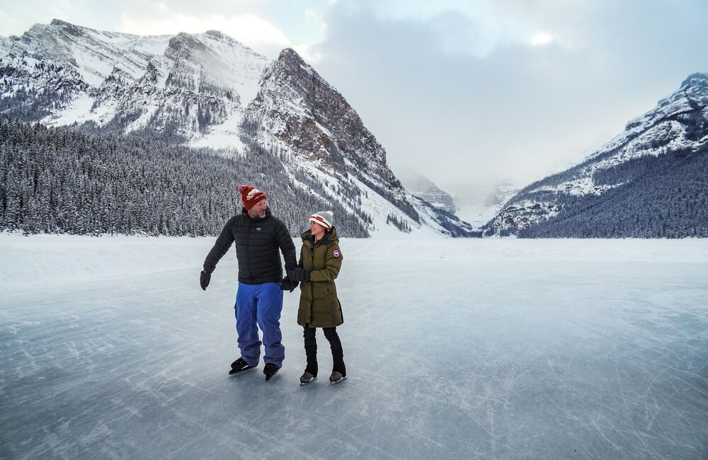 Two people skate on a frozen Lake Louise with Victoria Glacier in the background