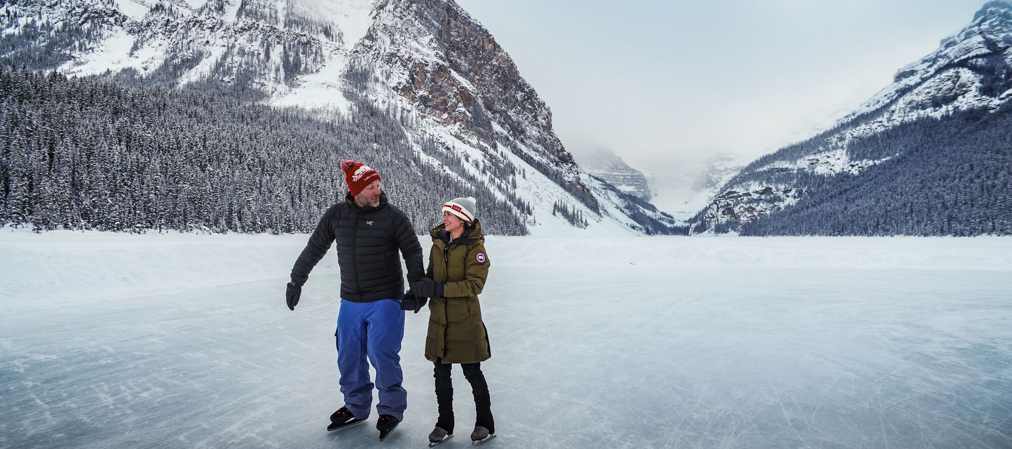 Two people skate on a frozen Lake Louise with Victoria Glacier in the background