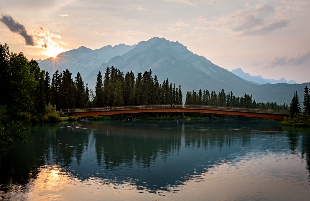 The Nancy Pauw Bridge in Banff at sunset with a river in the front and Mt. Norquay in the background.