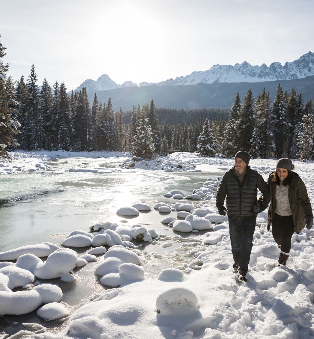 A couple walking along the Bow river in spring with snow in Banff National Park