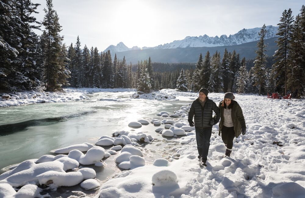 A couple walking along the Bow river in spring with snow in Banff National Park