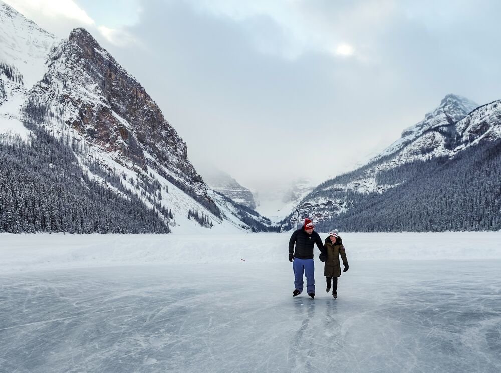 Two people skate on a frozen Lake Louise with Victoria Glacier in the background