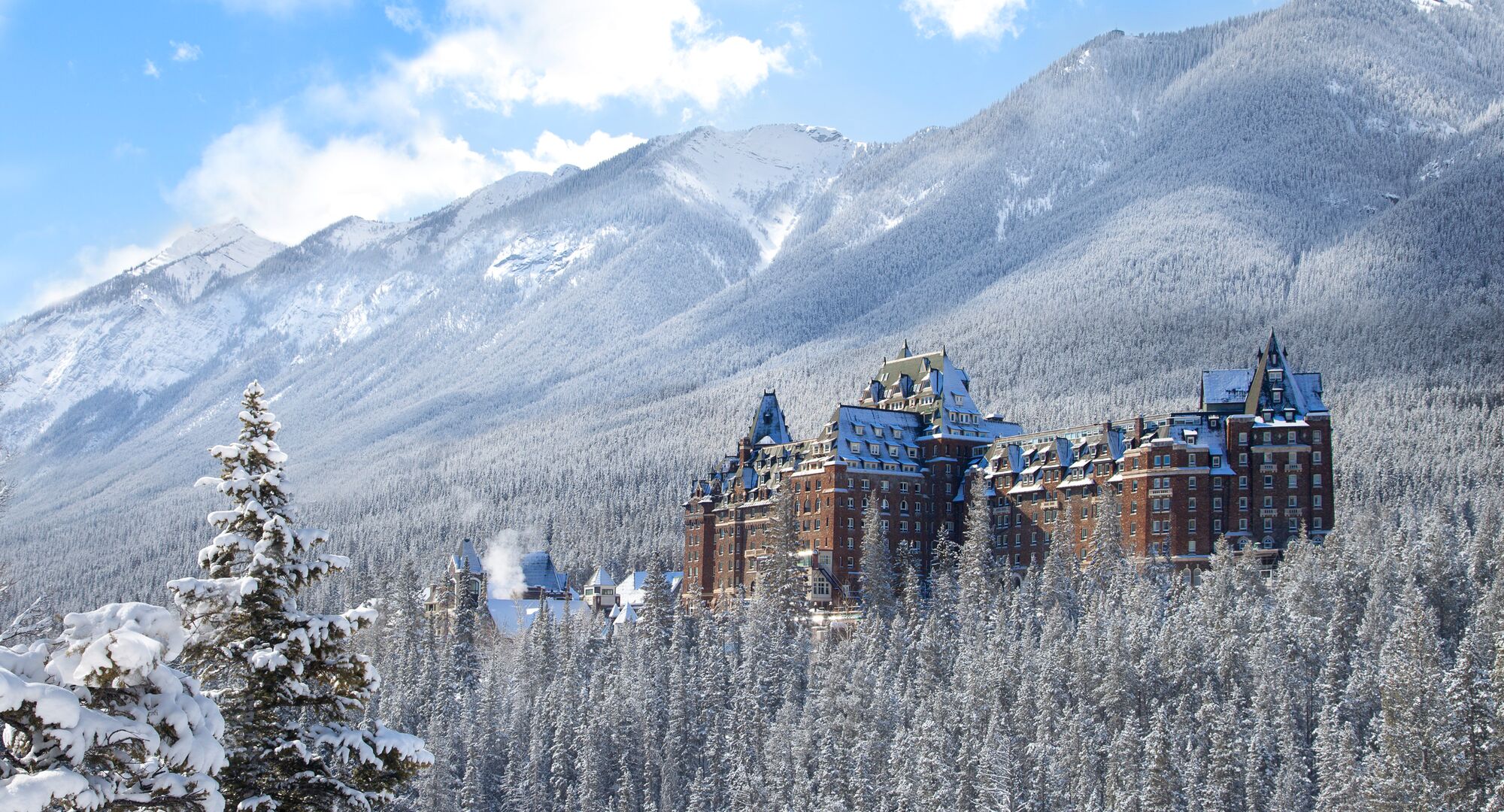 Fairmont Banff Springs - the Castle of the Rockies towering above the snowy forest on a crisp winter day in Banff National Park. 