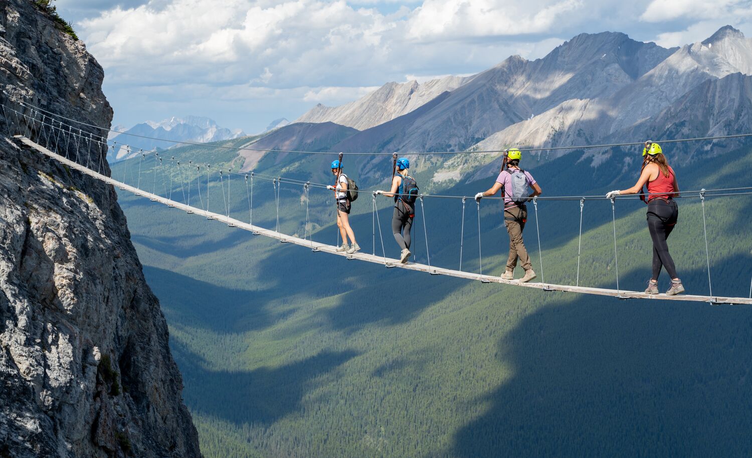 Four people walking across a bridge on the Via Ferrata at Mount Norquay in Banff National Park