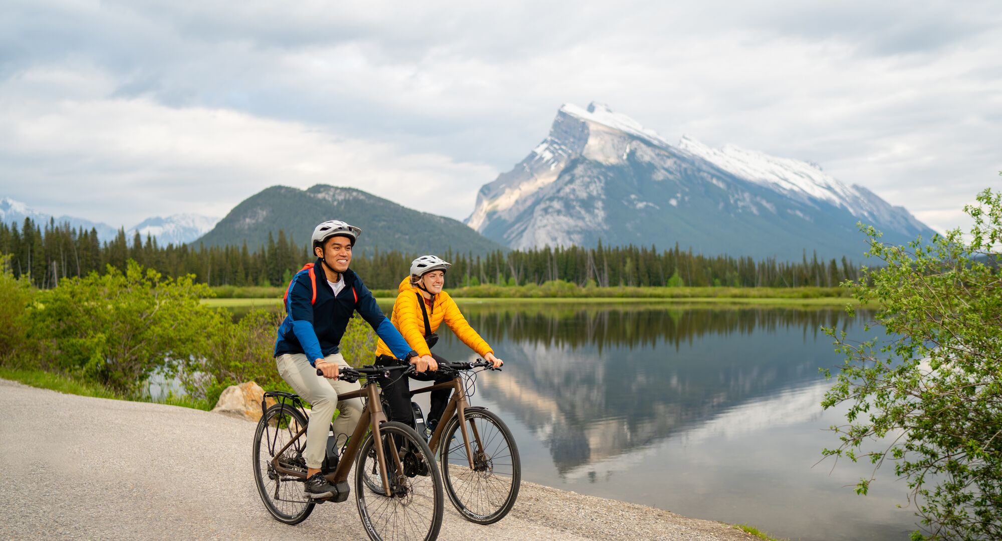 Two people biking Vermilion Lakes Drive with a view of Mount Rundle in the background