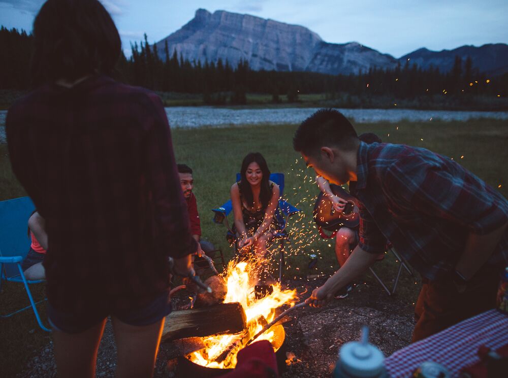 Friends sit around the campfire at Cascade Ponds with Mount Rundle in the background in Banff National Park.