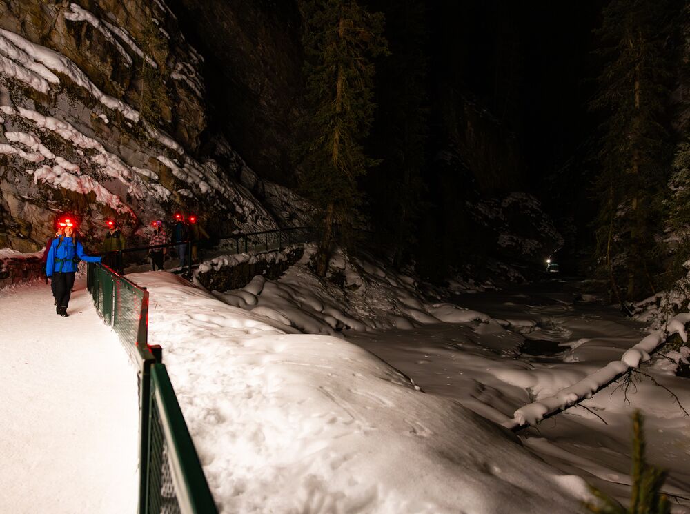 A group of people walk in Johnston Canyon at night in Banff National Park.
