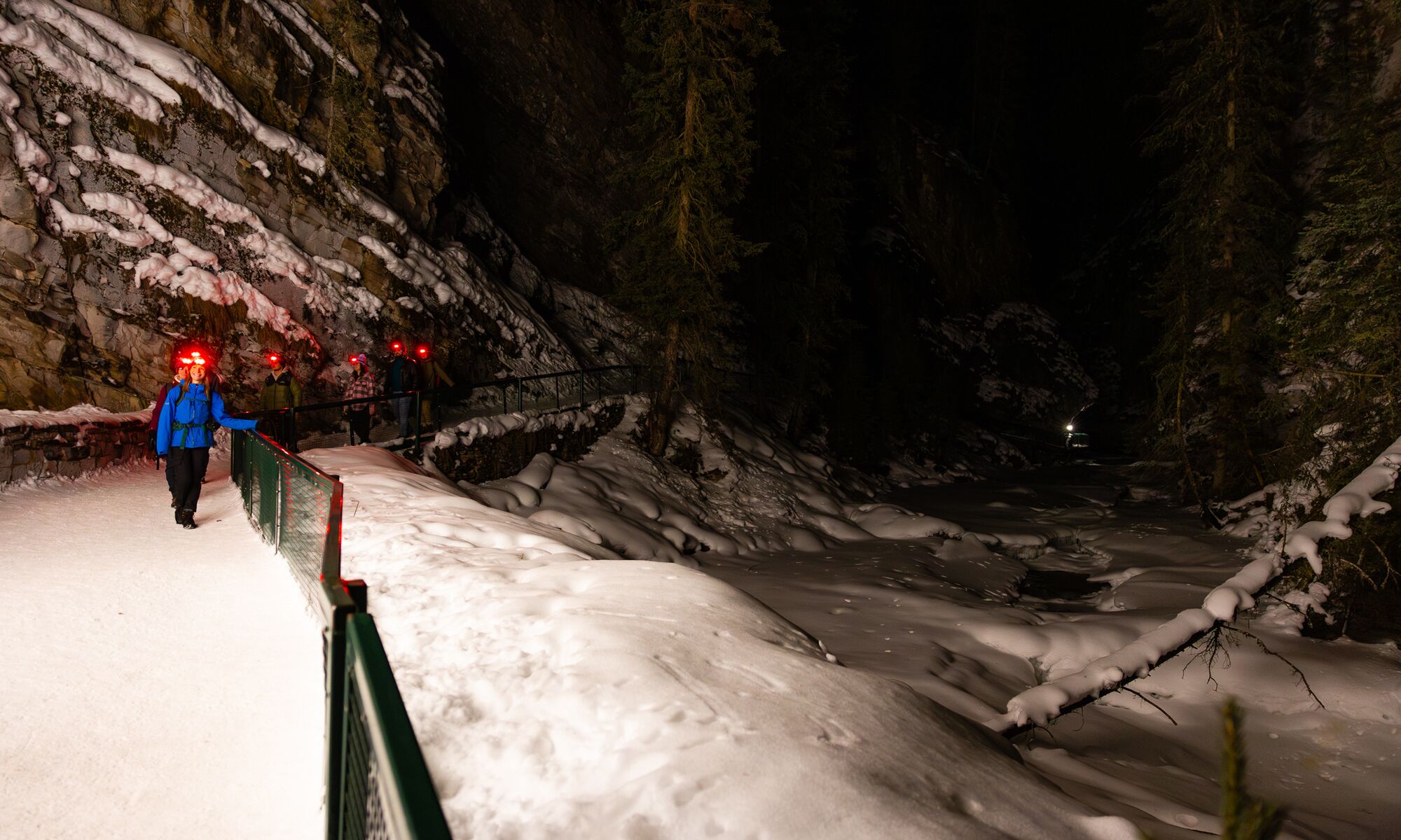 A group of people walk in Johnston Canyon at night in Banff National Park.