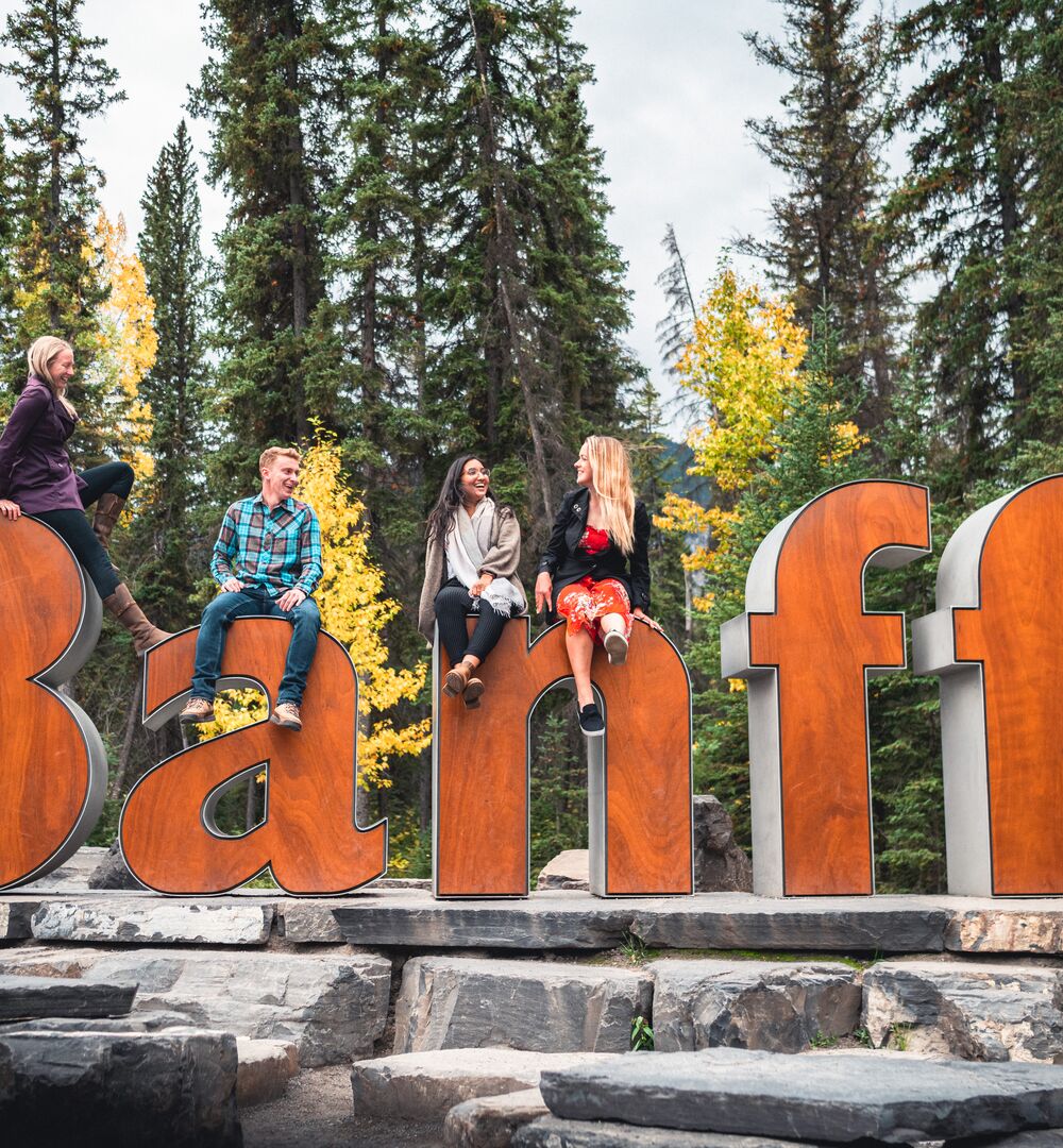 A group of friends sitting on the Banff Sign for a photo