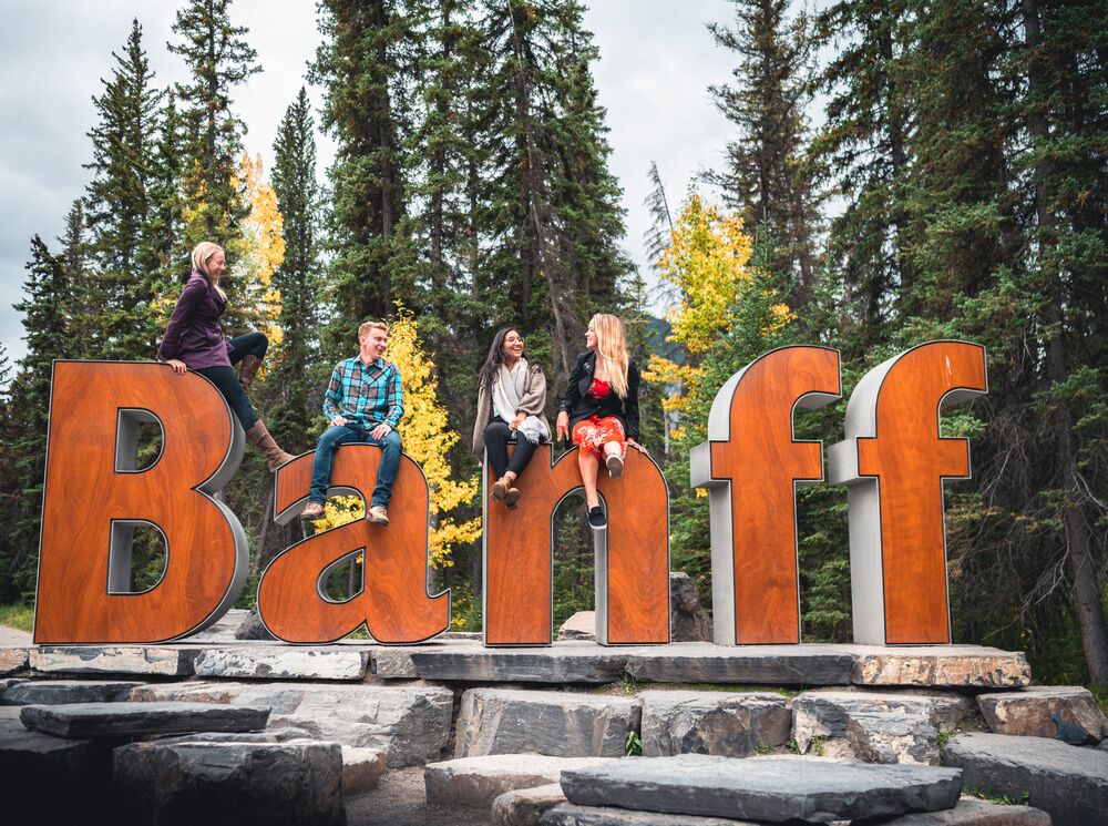 A group of friends sitting on the Banff Sign for a photo