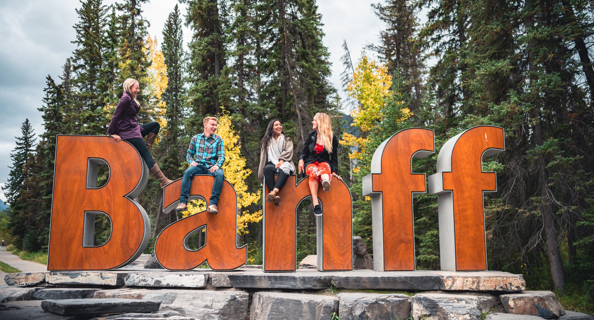 A group of friends sitting on the Banff Sign for a photo