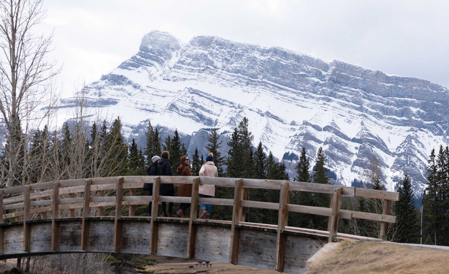 A group of people stand on a bridge looking at Mount Rundle from Cascade Ponds in Banff National Park.