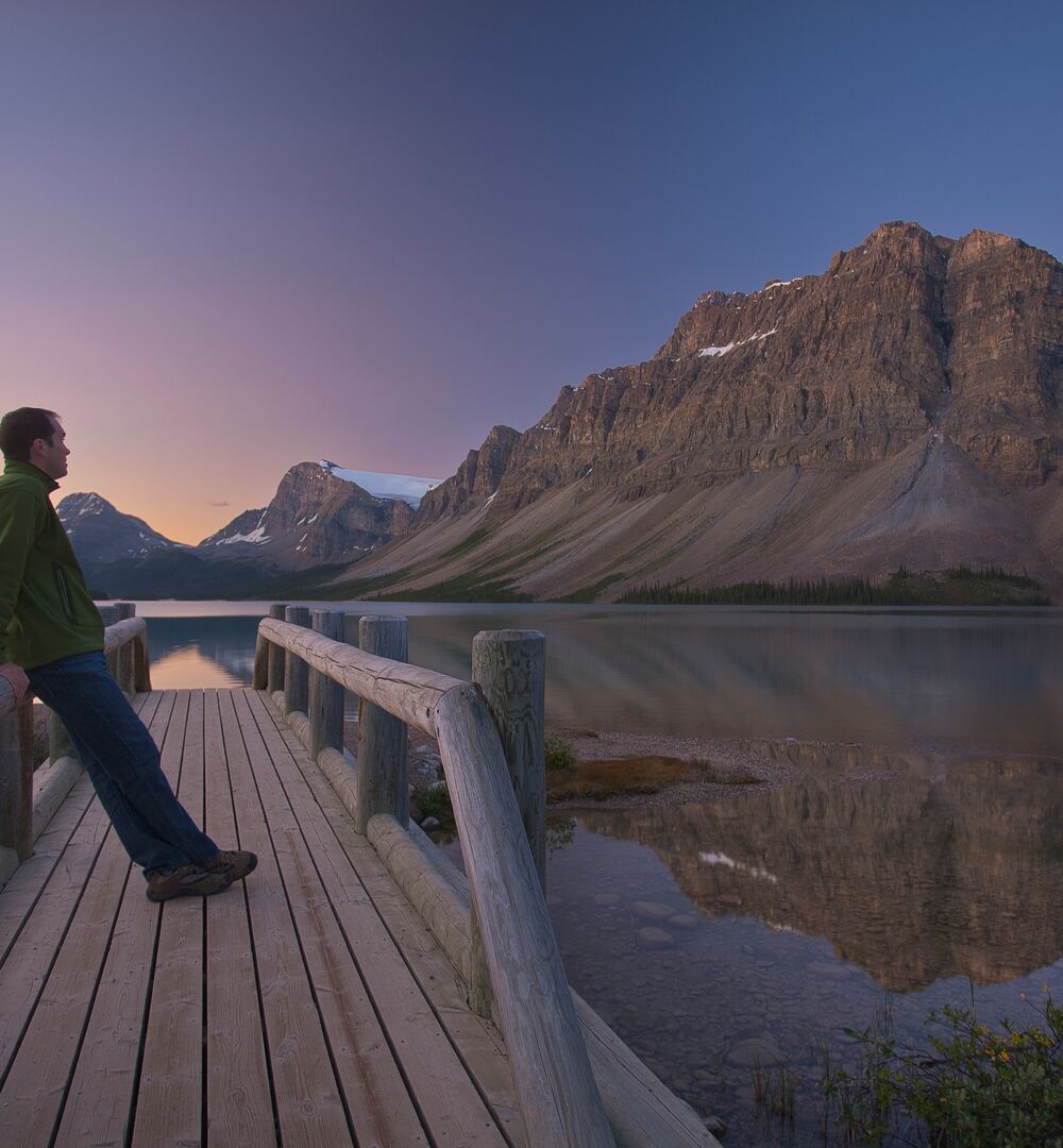 A person looks at Bow Lake from the bridge during sunrise in the summer.