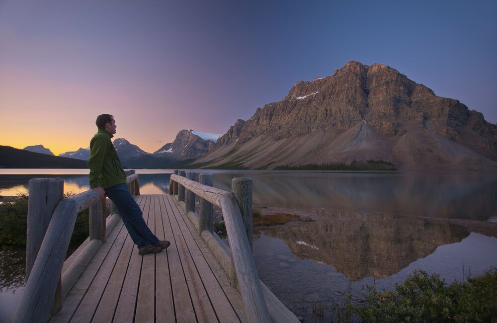 A man stands on the bridge at Bow Lake at sunrise in Banff National Park.
