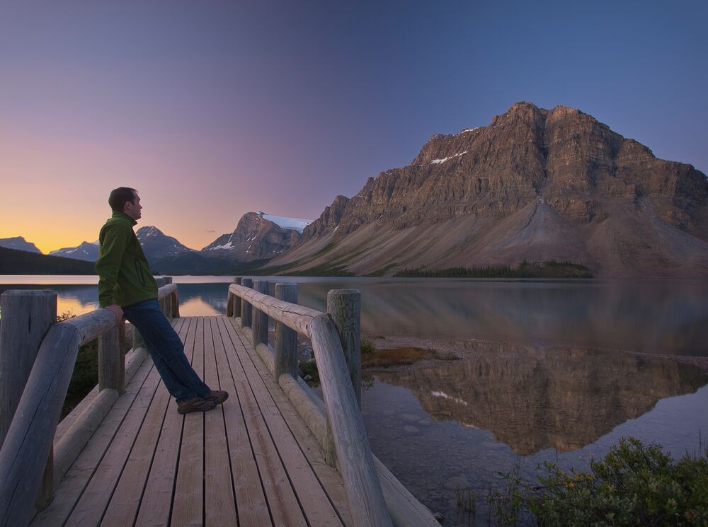 A man stands on the bridge at Bow Lake at sunrise in Banff National Park.