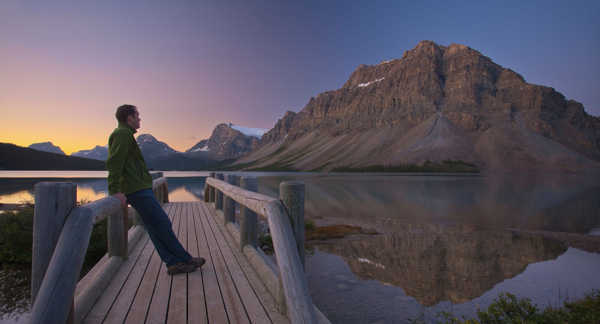 A person looks at Bow Lake from the bridge during sunrise in the summer.