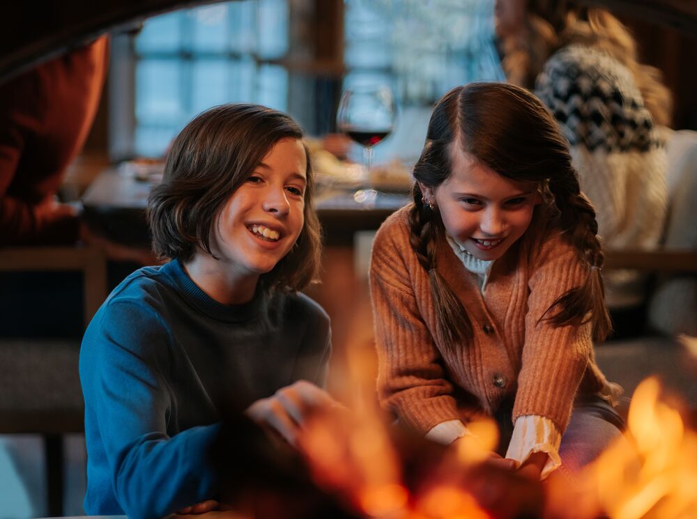 Two kids sit in front of a fireplace at Bluebird Steakhouse in Banff.