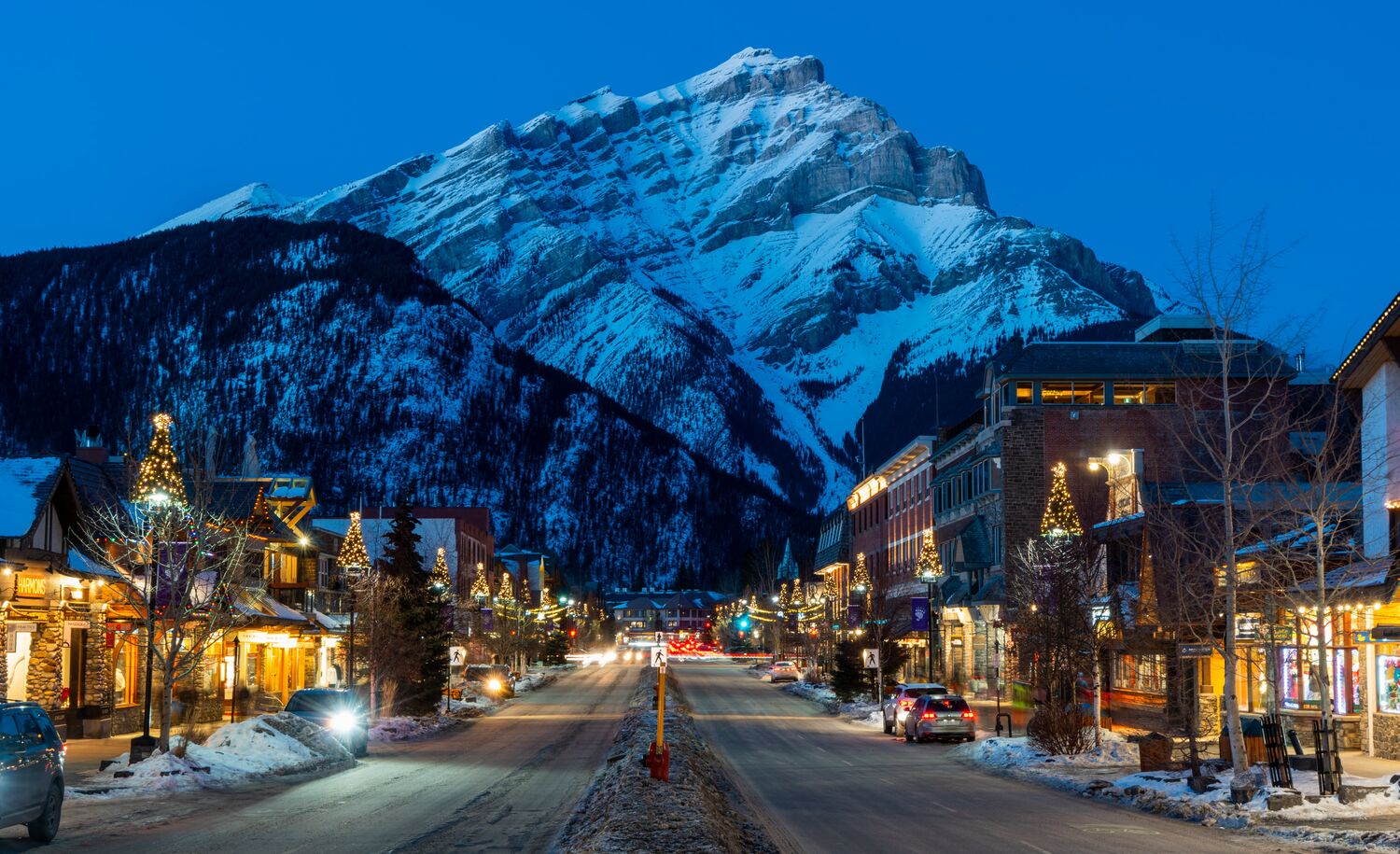 Cascade Mountain rises above Banff Avenue, which features many Banff restaurants, in the winter at blue hour in  Banff, Canada.
