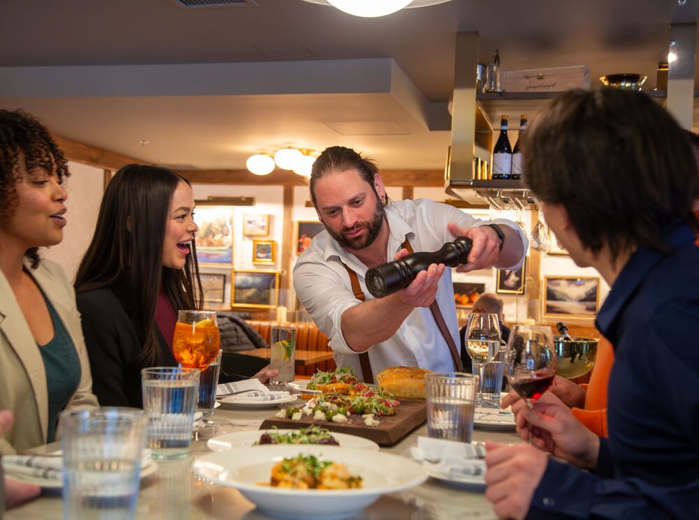 A group of people enjoy watching a server finish a meal tableside at The Fat Ox in Banff.