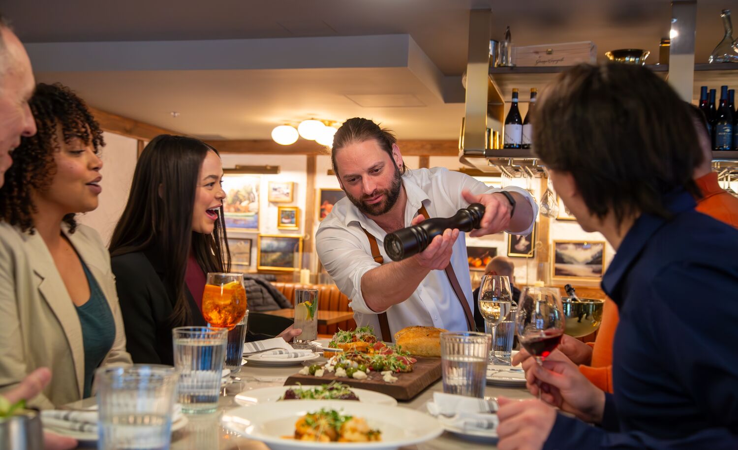 A group of people enjoy watching a server finish a meal tableside at The Fat Ox in Banff.