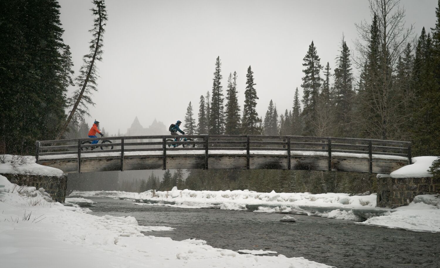 Two people bike over a bridge on the Spray River Trail in Banff National Park in winter.