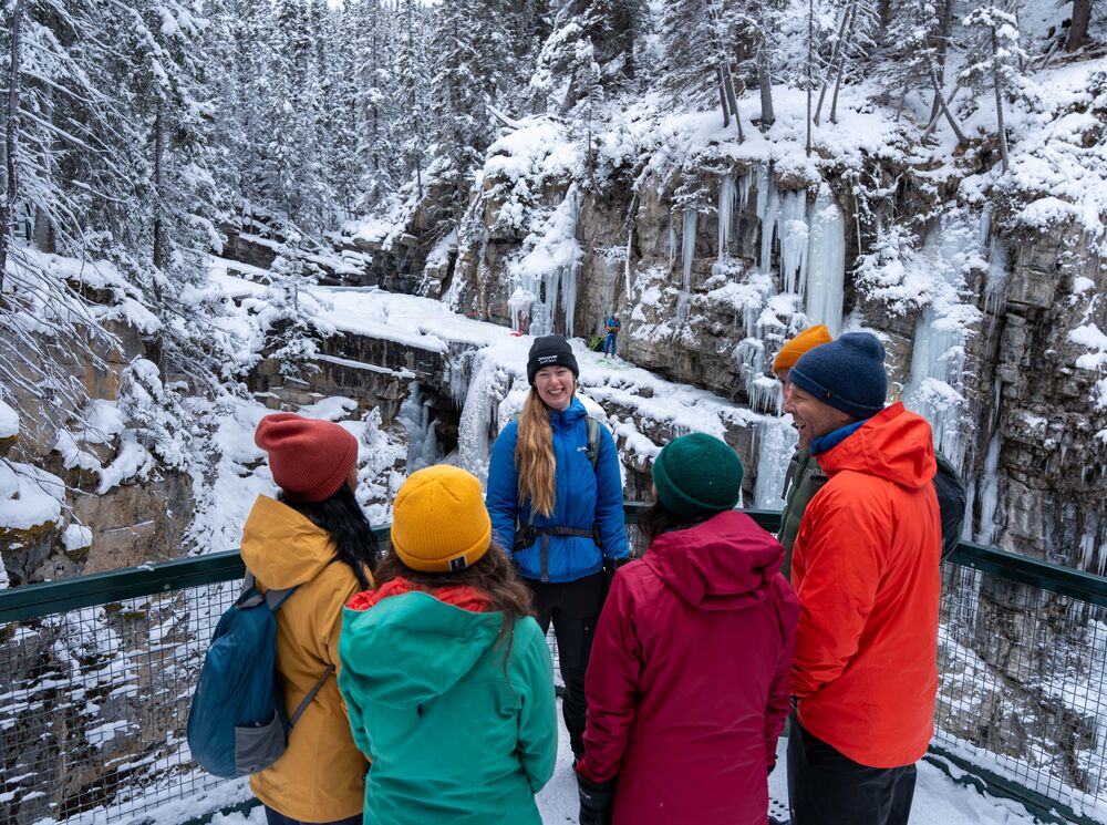 A group of people talk to a guide at Johnston Canyon in the winter at the upper falls in Banff National Park.