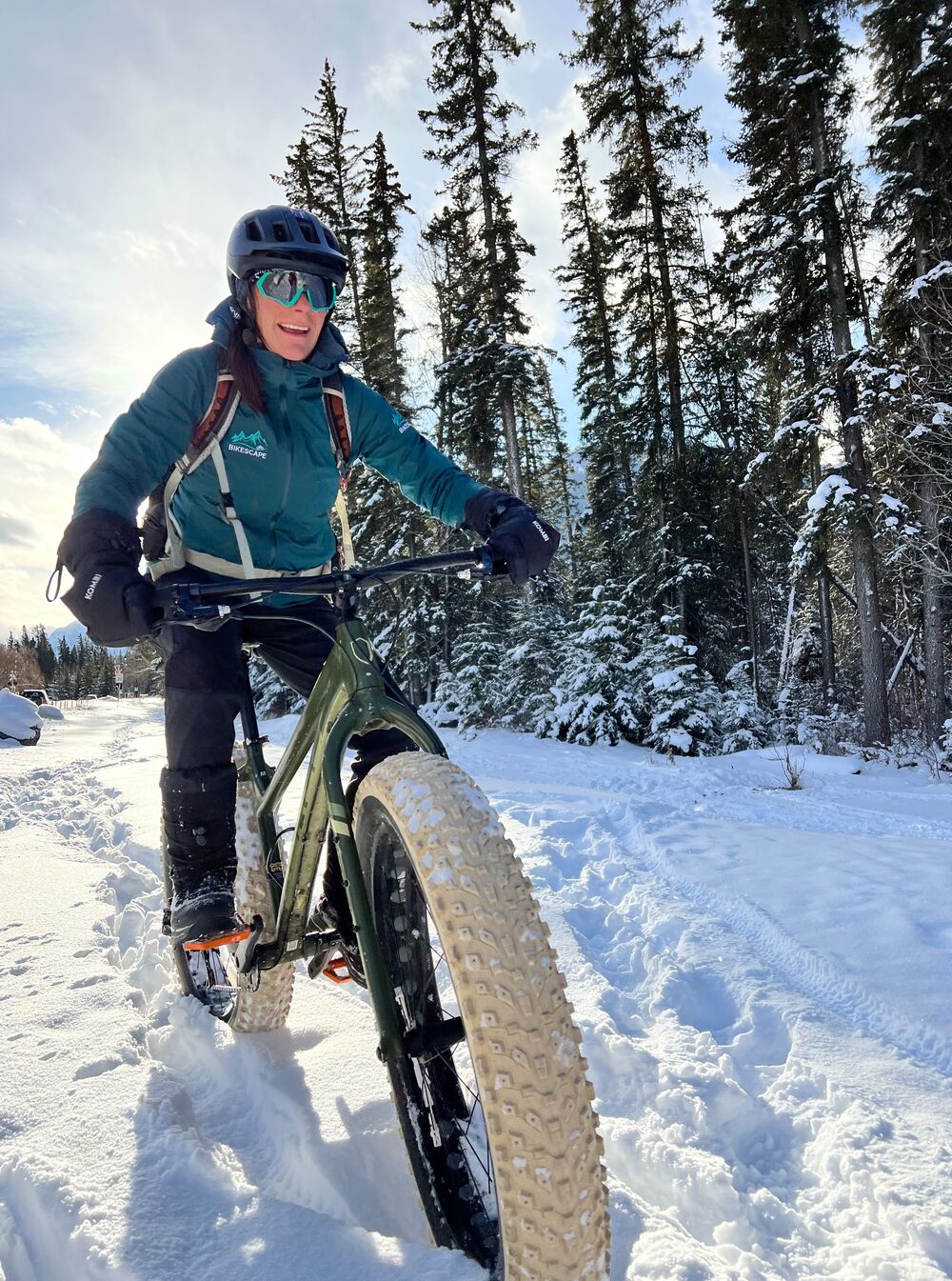 A fat biker rides in the snow through trees in Banff National Park.