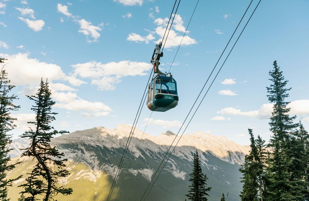 A gondola car goes up the cable with Mount Rundle in the background