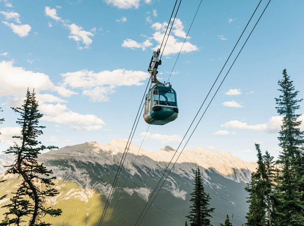 A gondola car goes up the cable with Mount Rundle in the background