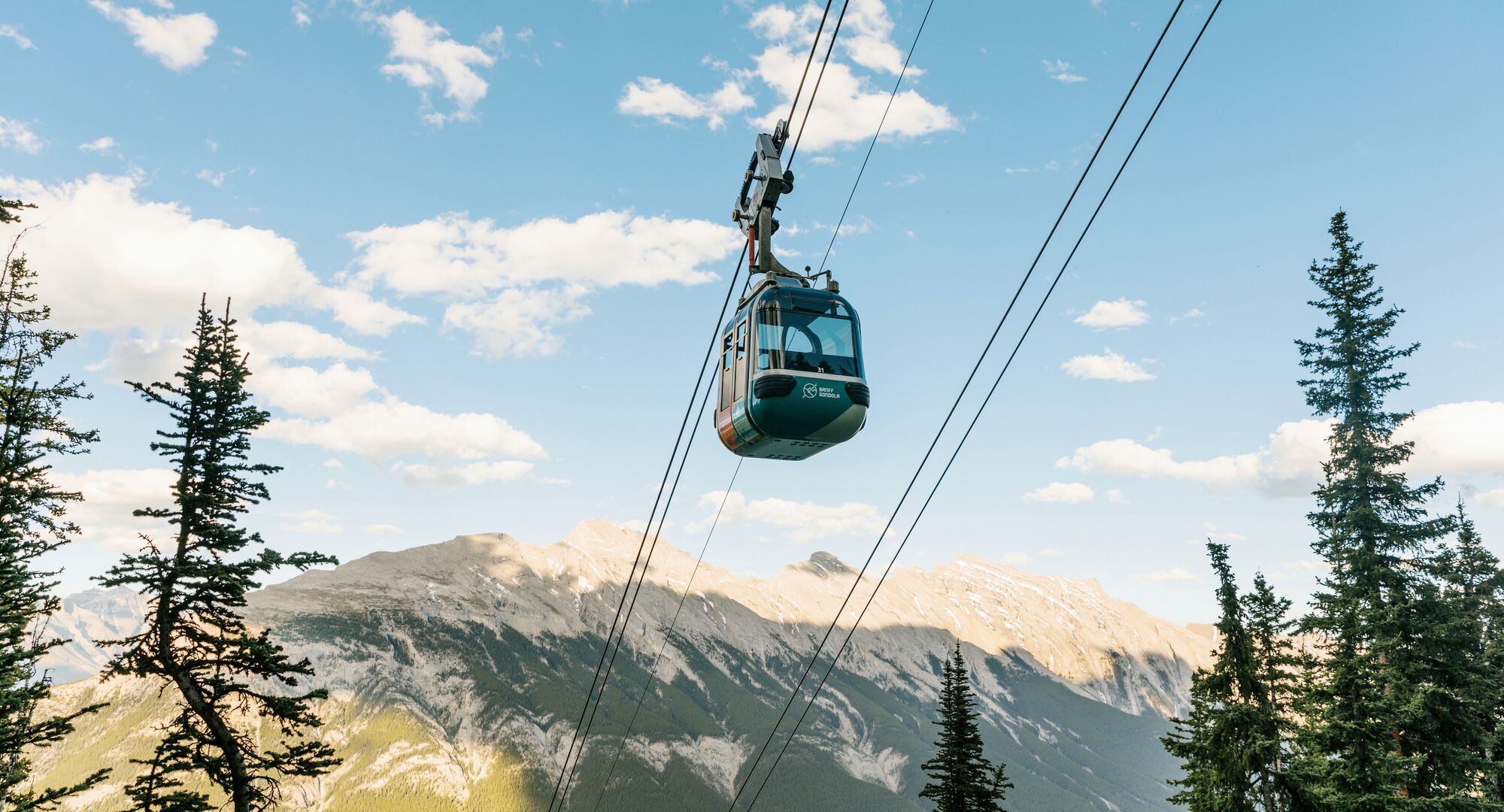 A gondola car goes up the cable with Mount Rundle in the background