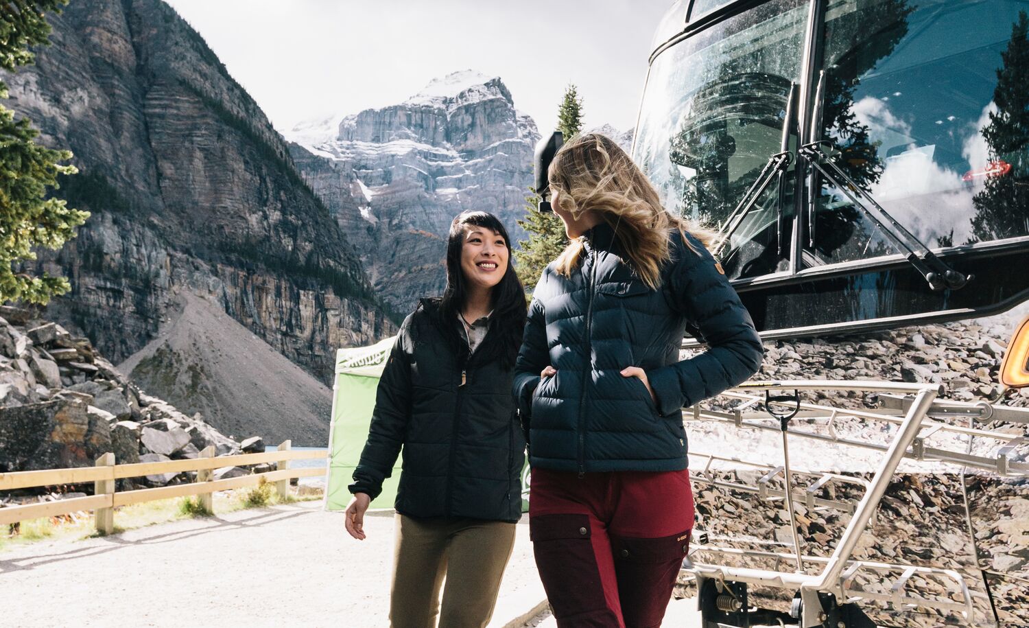 Two people in front of the Roam Public Transit bus at Moraine Lake on a sunny fall day in Banff National Park.