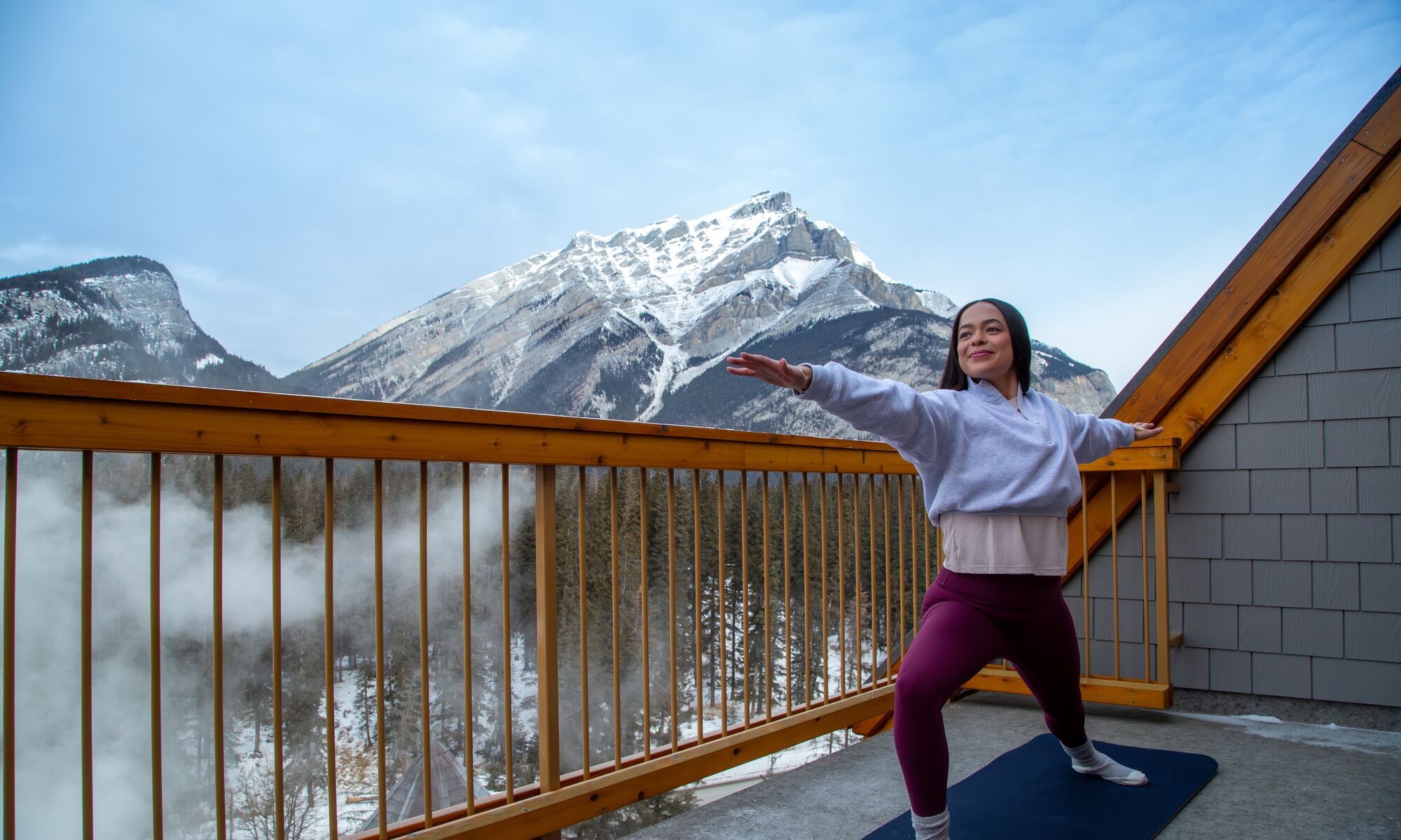 Solo female on balcony doing yoga with Cascade Mountain in the background in Banff National Park