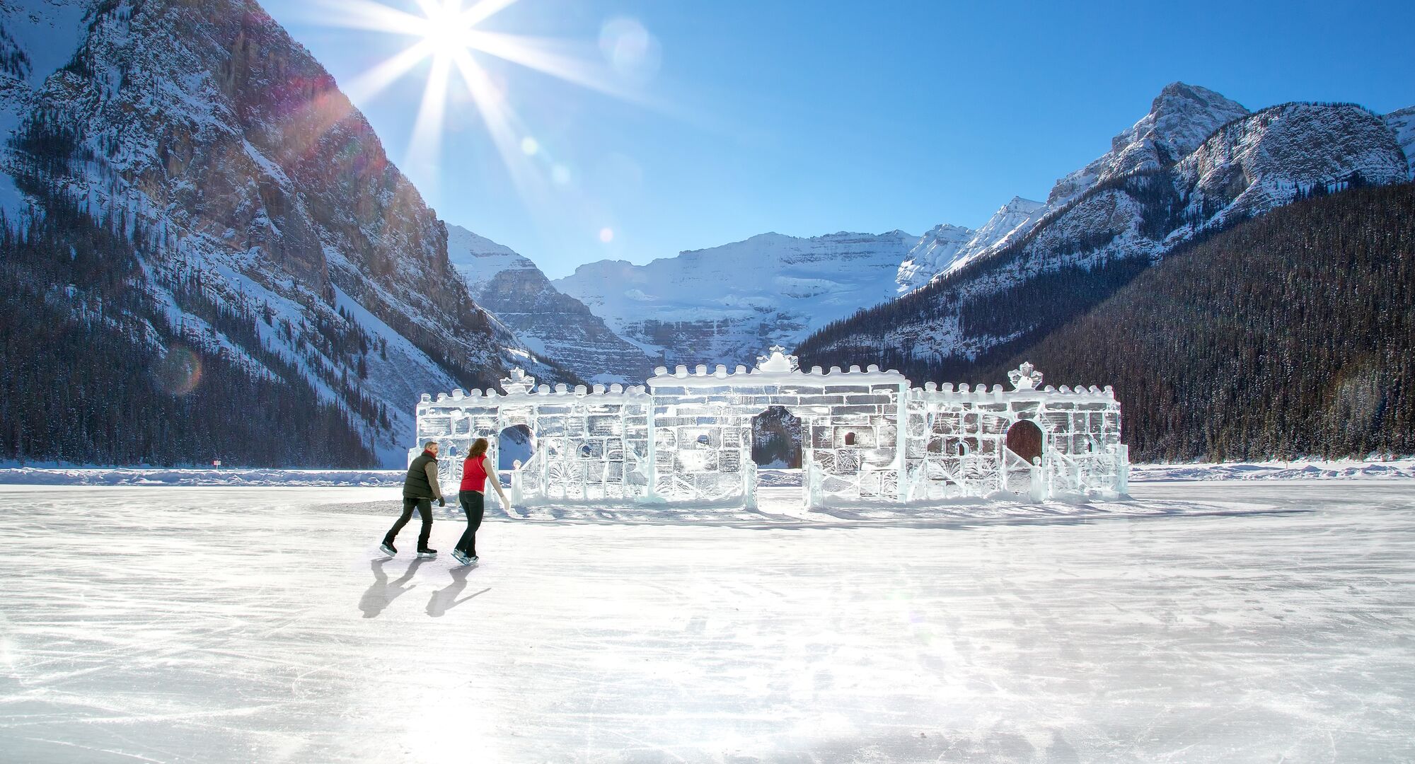 Two people skating on the ice rink on Lake Louise with an ice castle and glacier in the background