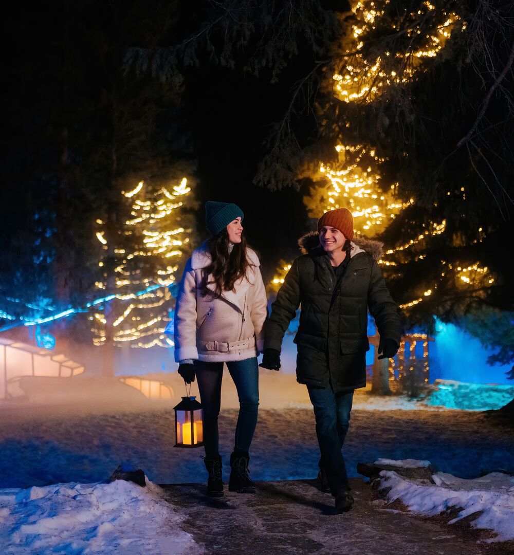 A couple walking through a lit up Cascade of Times Garden for In Search of Christmas Spirit in Banff