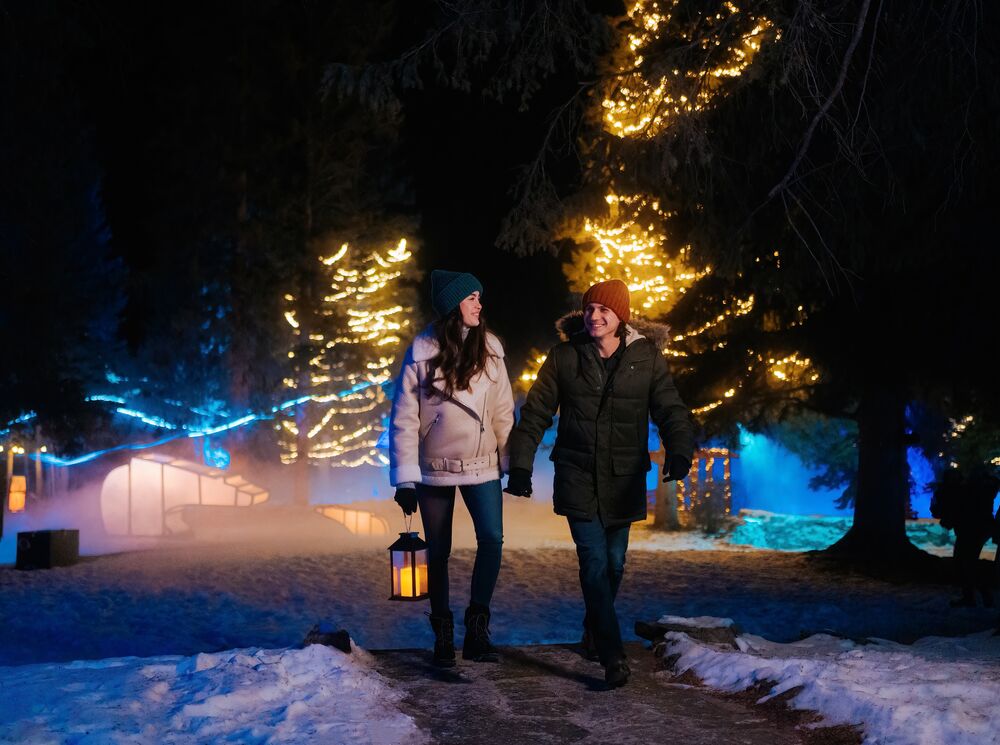 A couple walking through a lit up Cascade of Times Garden for In Search of Christmas Spirit in Banff