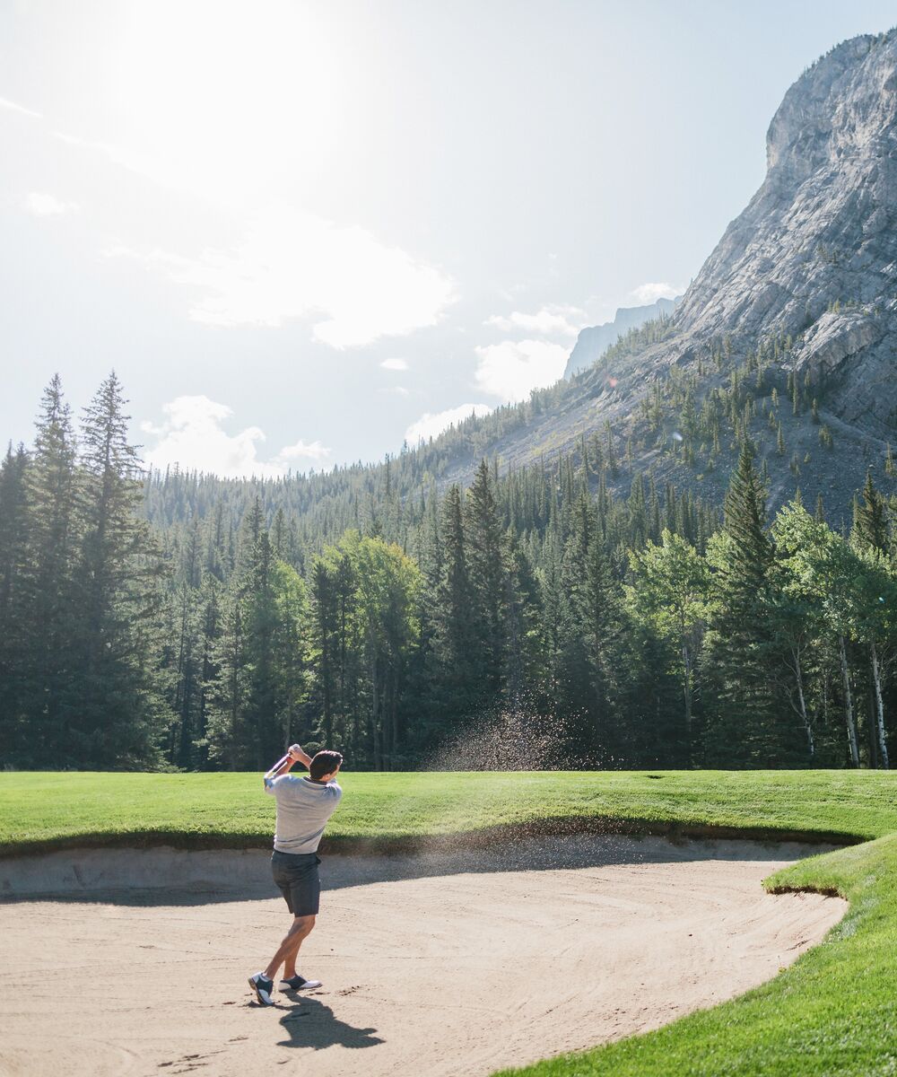A man playing golf at the Fairmont Banff Springs Golf Course on a sunny day surrounded by trees and mountains