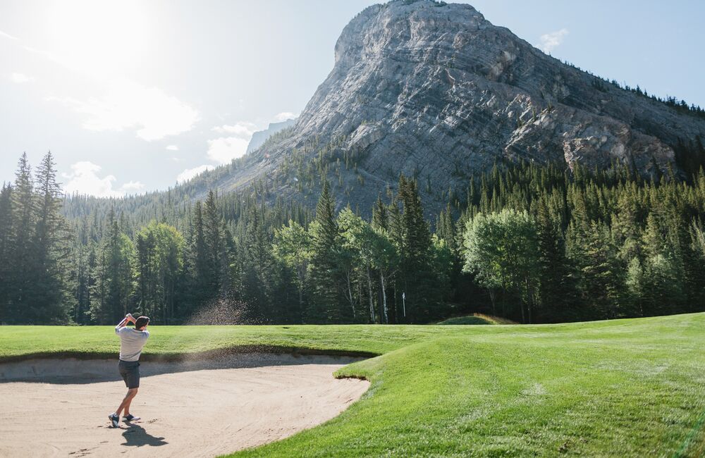 A man playing golf at the Fairmont Banff Springs Golf Course on a sunny day surrounded by trees and mountains