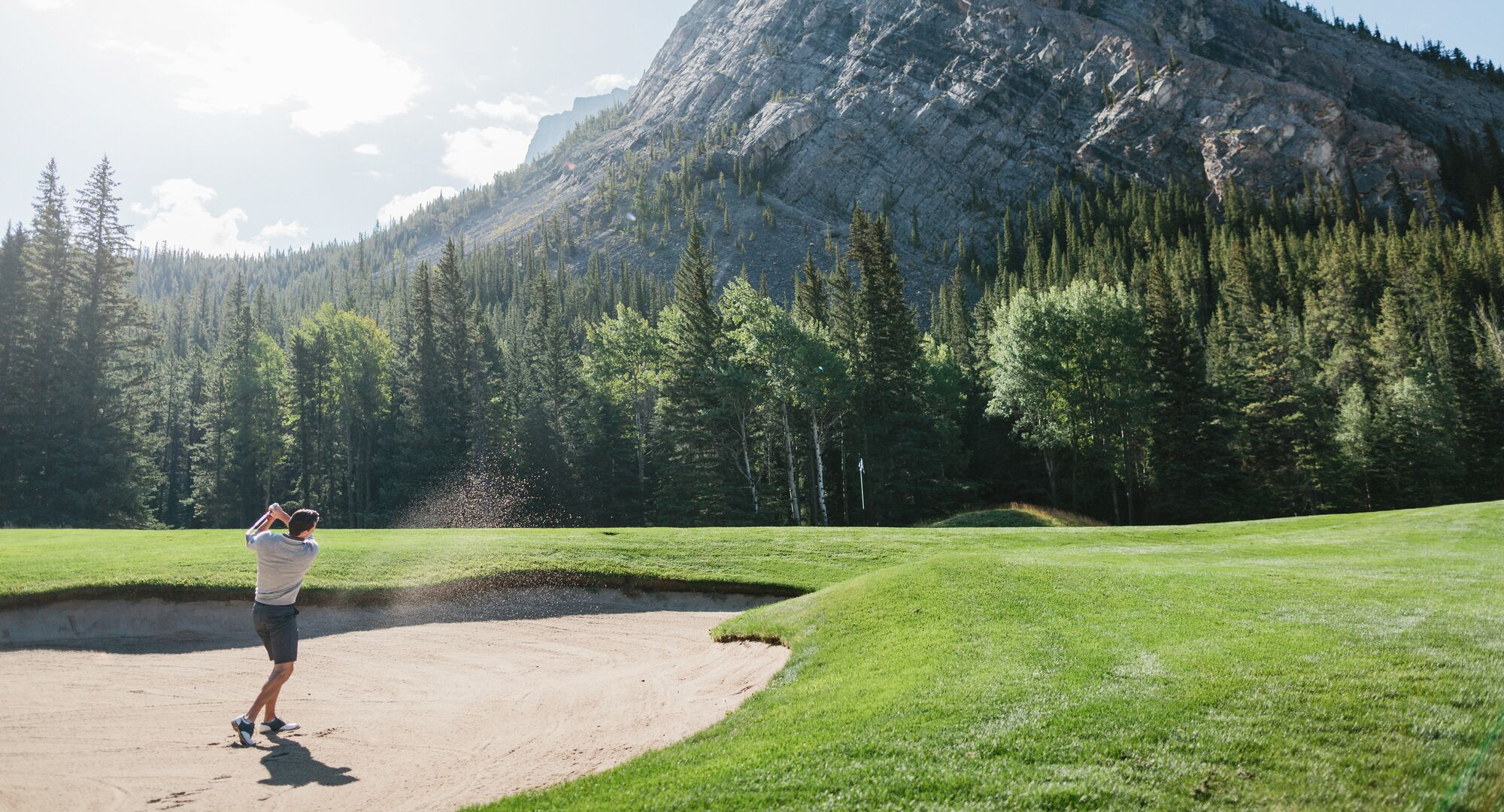 A man playing golf at the Fairmont Banff Springs Golf Course on a sunny day surrounded by trees and mountains