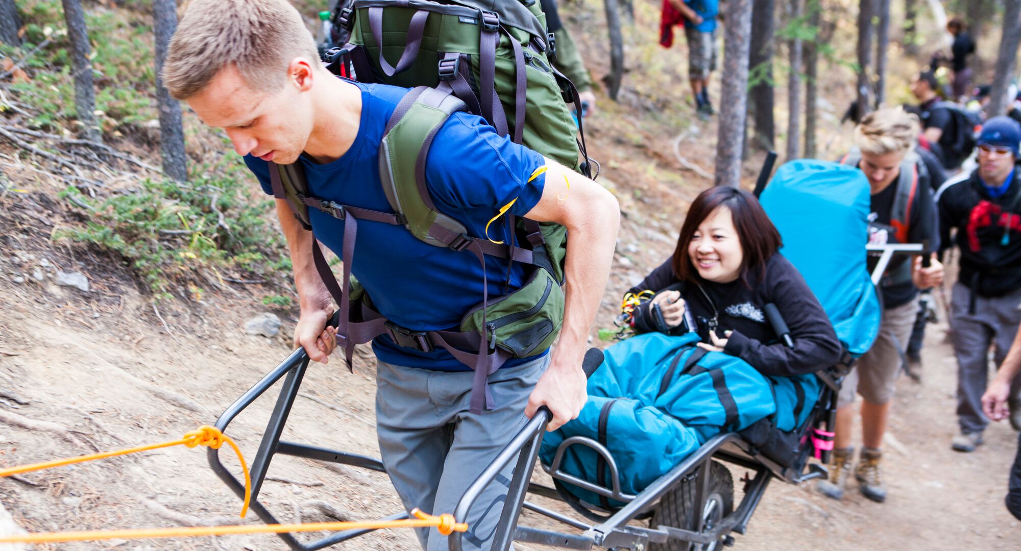 A group of people hiking on a trail assisting a person with disability on the trail