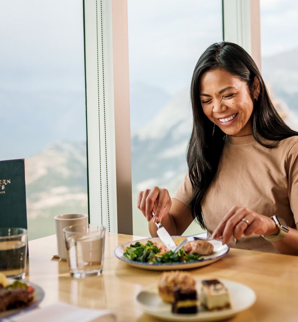 A woman enjoys a salad and desert while looking at the mountain views from Northern Lights Bistro at the Banff Gondola while being thoughtful about dietary restrictions in Banff National Park.