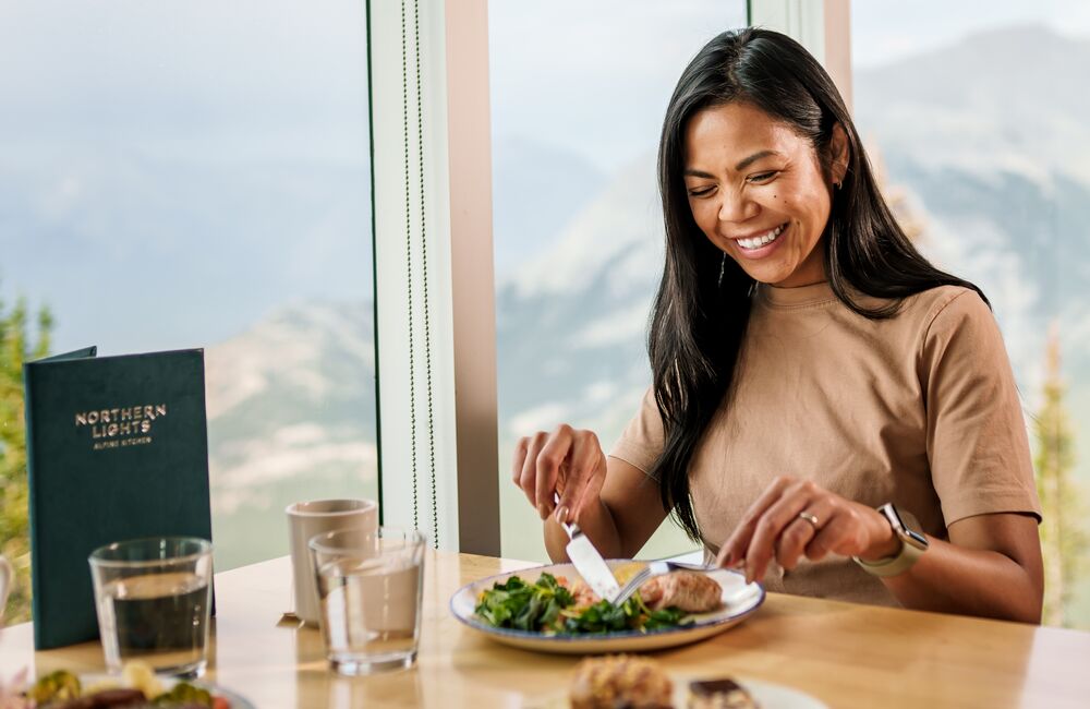 A woman enjoys a salad and desert while looking at the mountain views from Northern Lights Bistro at the Banff Gondola while being thoughtful about dietary restrictions in Banff National Park.