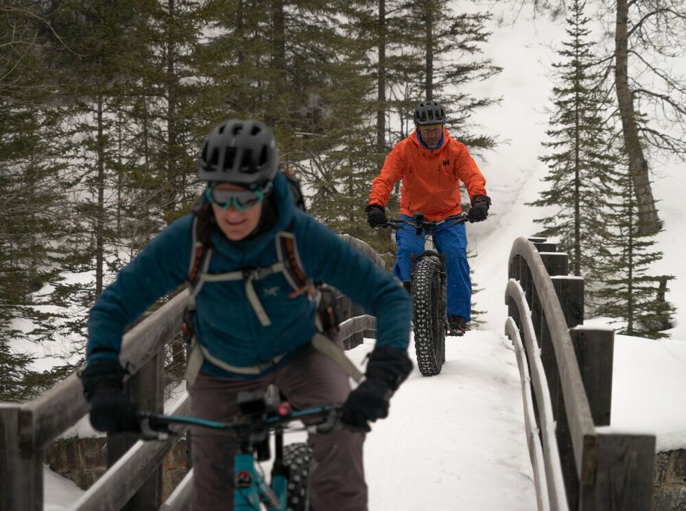 Two people bike across a bridge on the Spray River Trail in Banff National Park.