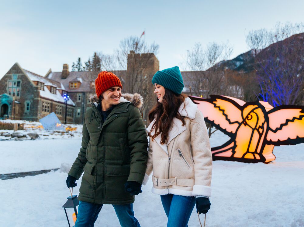 A couple walking through a lit up Cascade of Times Garden for In Search of Christmas Spirit in Banff